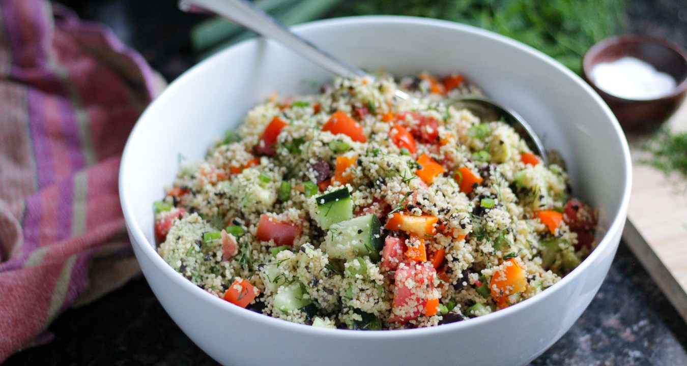 Couscous mixed with chopped vegetables served in a white serving bowl.